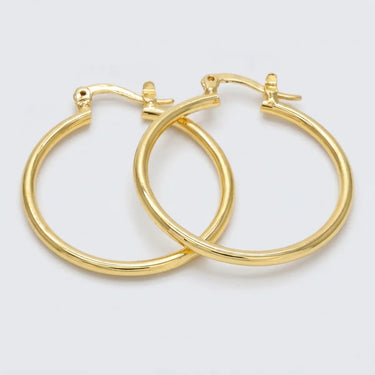 Polished gold hoop earrings with a sleek rounded silhouette and secure latch closure on a light neutral background - Matte Jewelry