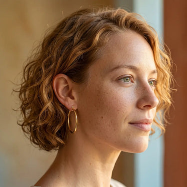 Woman wearing polished gold hoop earrings with a sleek lightweight design, styled in a natural lifestyle portrait with soft warm lighting - Matte Jewelry