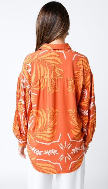 Maréa Blouse back view showing loose drape and full tropical print design across the fabric, long sleeves with relaxed fit, styled with crisp white pants for a resort-inspired outfit.
