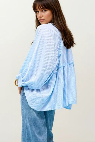 Woman wearing a light blue checkered blouse with ruffled sleeves on a plain background
