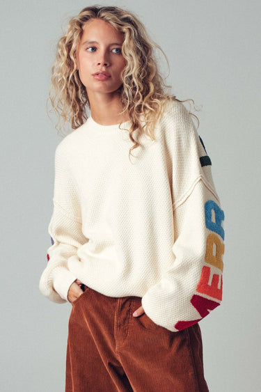 Woman wearing a white sweater with colorful letter sleeves against a gray background