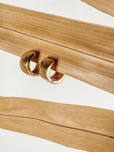 A close-up image of a pair of Mila gold-plated hoop earrings on a wooden surface.