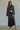 A woman wearing a long-sleeve crop satin top in black, paired with a high-waisted skirt with a side slit.