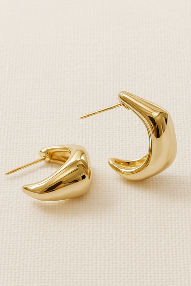 Gold plated sculptural hoop earrings with curved shape on white background.