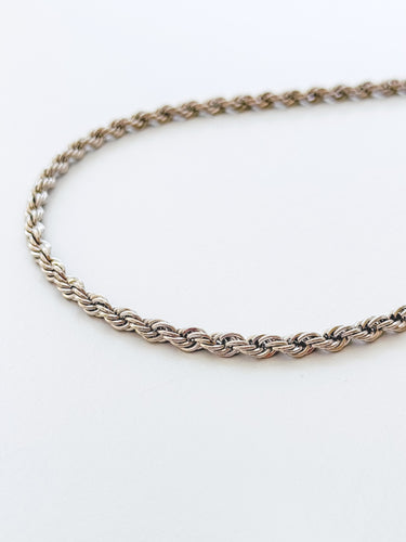 A gold-plated necklace with a rope chain design, laid out on a plain surface.