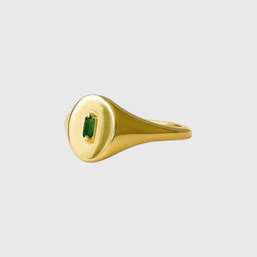 Gold Montego ring with a green gemstone on a beige background