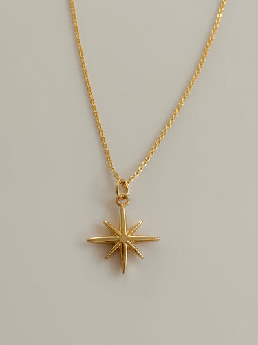 Close-up of Nova Necklace showing polished gold star pendant and delicate chain.