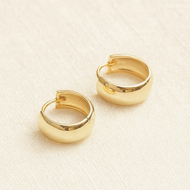 Nuage Huggie Earrings, gold chunky huggie hoop earrings with smooth rounded band and polished mirror finish, photographed on white linen background with soft editorial lighting.