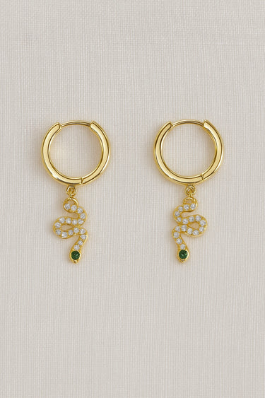 Opira Huggie Earrings — gold plated huggies with serpent charm, white crystals and green stone eye on linen background, elegant and symbolic jewelry by Matte.