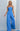 Model wearing the Oriana Jumpsuit in bright blue strapless wide-leg design against a light gray background.