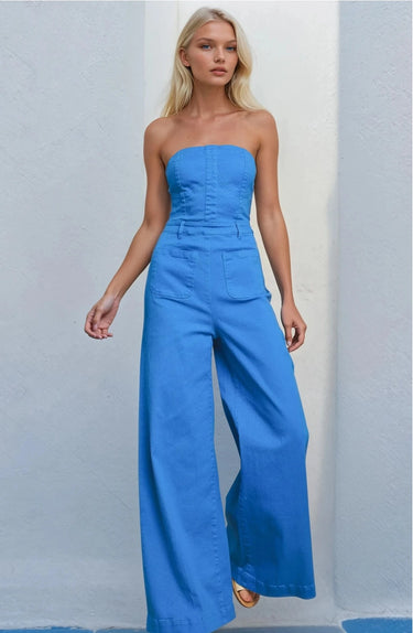 Model wearing the Oriana Jumpsuit in bright blue strapless wide-leg design against a light gray background.