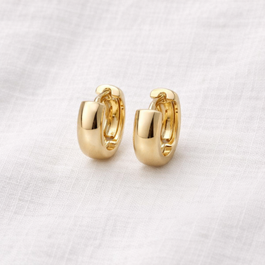 Orix Huggie Earrings – chunky gold huggie earrings with a smooth polished gold finish, photographed on a soft neutral background.
