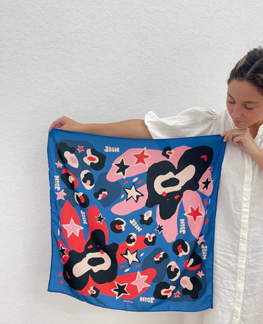 Periwi Scarf in periwinkle blue, pink, and coral abstract print, silky square scarf held by model in white dress, Matte Wrap It Up collection.