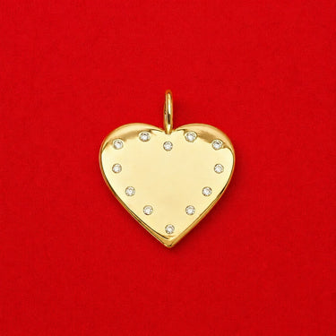 Pola Pendant gold heart charm with clear zirconia stones on a polished surface, photographed on a bold red background