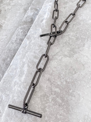 A black enamel necklace with a chain link design, displayed on a textured surface.
