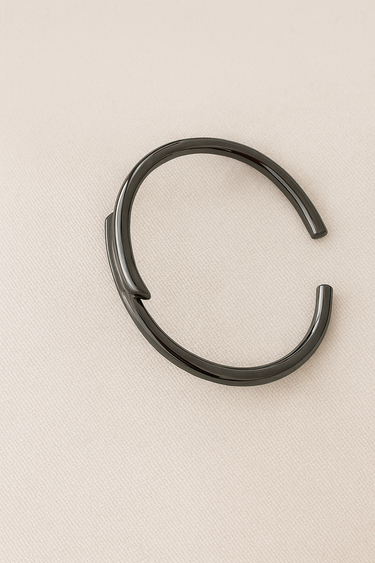 Gunmetal open cuff bracelet with sculptural design on beige linen background.
