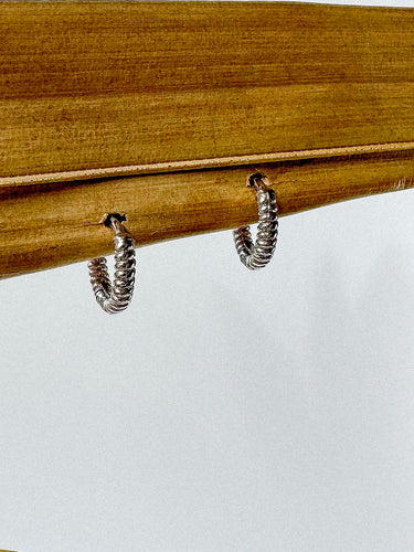 A pair of Sabina gold-plated huggie earrings displayed on a wooden surface.