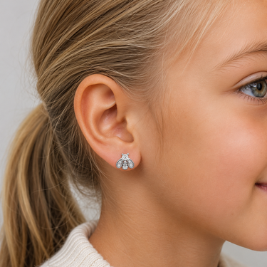 Young blonde girl wearing Silver Bee Stud. Earrings with sparkling crystal wings and polished silver finish in a soft close-up portrait with neutral studio lighting.
