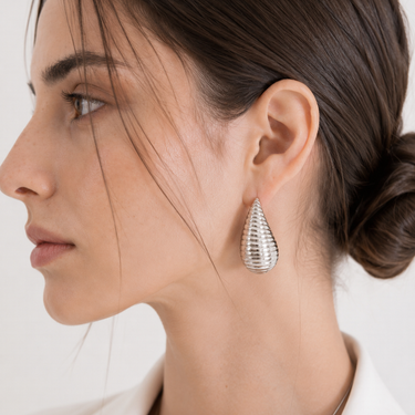Silver Ribbed Teardrop Statement Earrings worn on model in side-profile close-up, featuring a sculptural polished silver finish and textured ridged design.