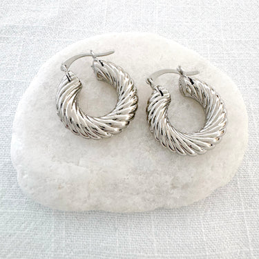 Sweet Huggie Earrings in a polished twisted hoop design on stone background.