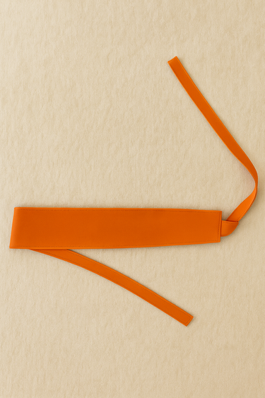 Tangerine wrap belt displayed flat on beige linen background.