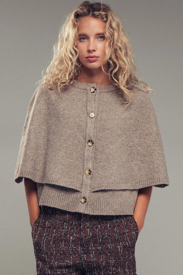 Model wearing neutral knit cape cardigan with oversized buttons and textured fabric, front view.