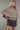 Woman wearing a brown knitted cape over a patterned outfit against a gray background