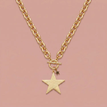 Close-up of model wearing Twinkle Necklace, a chunky gold chain necklace with oversized star pendant and small celestial charm, styled with a neutral knit top