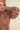 Brown blouse with intricate cut-out designs on sleeves and chest against a beige background