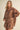 Woman wearing a brown embroidered outfit on a beige background