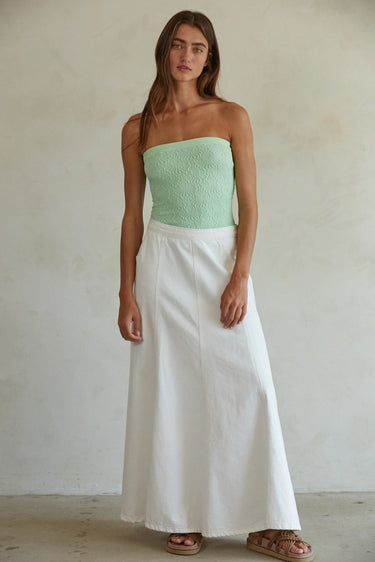 Woman wearing a strapless green top and white skirt against a plain background
