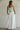 Woman wearing a strapless green top and white pants against a plain background