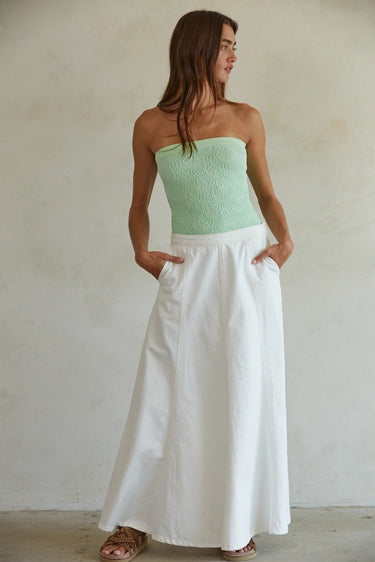 Woman wearing a strapless green top and white pants against a plain background