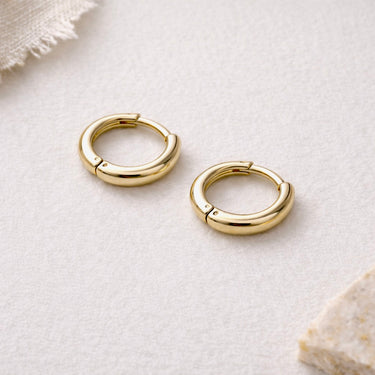 Velour Huggie Earrings gold huggie earrings on neutral fabric background.