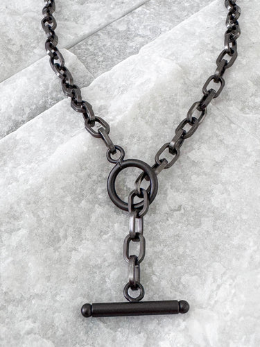 A black enamel necklace with a chain link design displayed against a textured grey background.