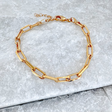 A gold-colored bracelet with a chain link design, displayed on a grey surface.