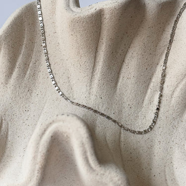 Aluna Necklace by Matte, silver flat chain on cream textured surface