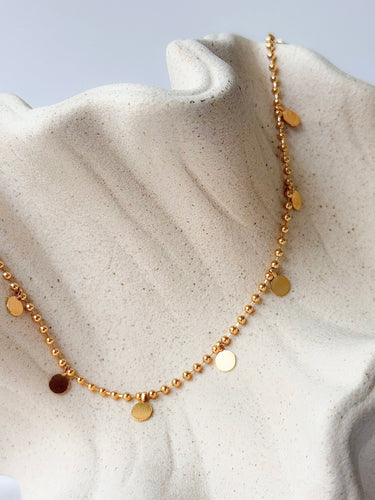 Aria Necklace by Matte, gold plated beaded necklace with disc charms on cream textured surface