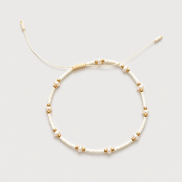 Arinet Bracelet in ivory featuring freshwater pearls, polished gold beads, and a cream adjustable cord.