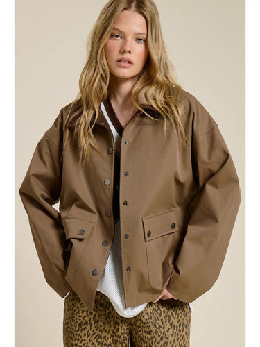 Model wearing the Aspen Utility Jacket in mocha brown featuring an oversized utility silhouette, snap-button front closure, oversized flap pockets, dropped shoulders, and long sleeves styled over a white top.