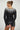 Back view of woman in black ribbed sweater with ombré white neckline detail, styled with a leather mini skirt, Aurora Sweater by Matte.