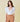 A woman wearing a white puff sleeve bodysuit with beige trousers, against a yellow background.