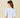 Model wearing the Azura Bodysuit in white — puff sleeve design with deep neckline, styled with camel trousers against a soft beige background, back view.