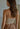 Model wearing the Glenn Top — beige ribbed shoulder-strap knit top with V-neckline, styled with printed skirt for a soft neutral look, back view.