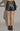 Black faux leather mini skirt with buckle waist detail styled with ankle boots — night-out look, back view.