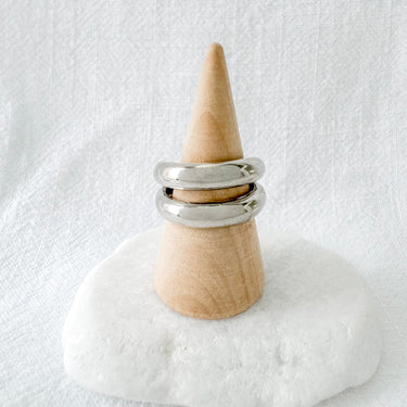 A two-band ring, featuring a silver and gold design, displayed on a wooden cone stand against a white background.