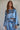 A woman wearing a long-sleeve crop satin top in blue, paired with a high-waisted skirt with a side slit.