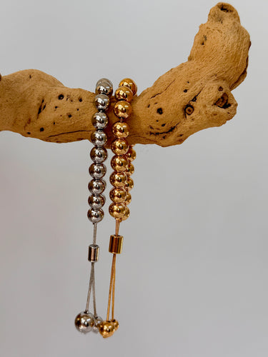 Adjustable Buda Bracelets in silver and gold polished beads on wood display