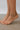 Silver beaded anklets on a person's feet with a neutral background