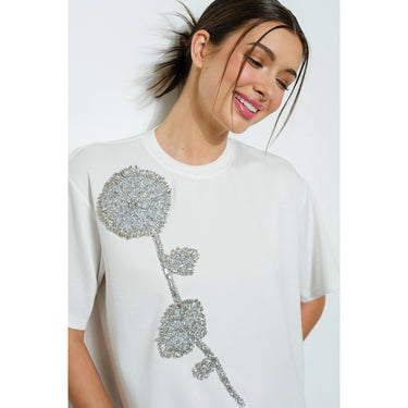 Woman wearing our Matte Capri crystal white t-shirt with silver floral design on a plain background